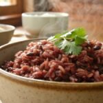 A bowl of perfectly cooked red rice with a fluffy texture, served in a rustic dish on a wooden counter