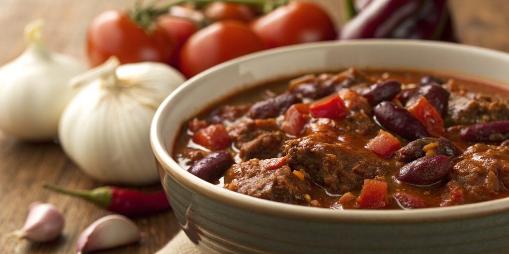 A close-up of venison chili with kidney beans, tomatoes, and spices in a rustic bowl.
